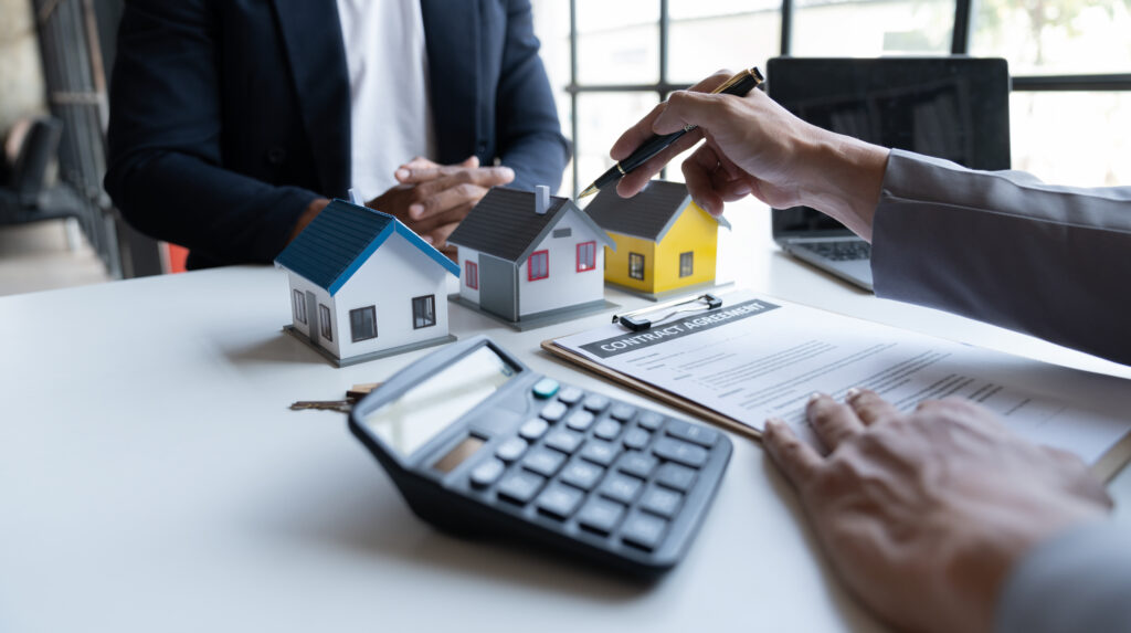 Two young Asian businessmen or architects are describing architectural house model in their office together for the construction of housing estate project in prime location the location is perfect